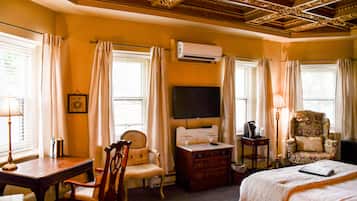 Una habitación de hotel con un escritorio de madera, una silla, una cama con edredón blanco, un televisor y un equipo de aire acondicionado.