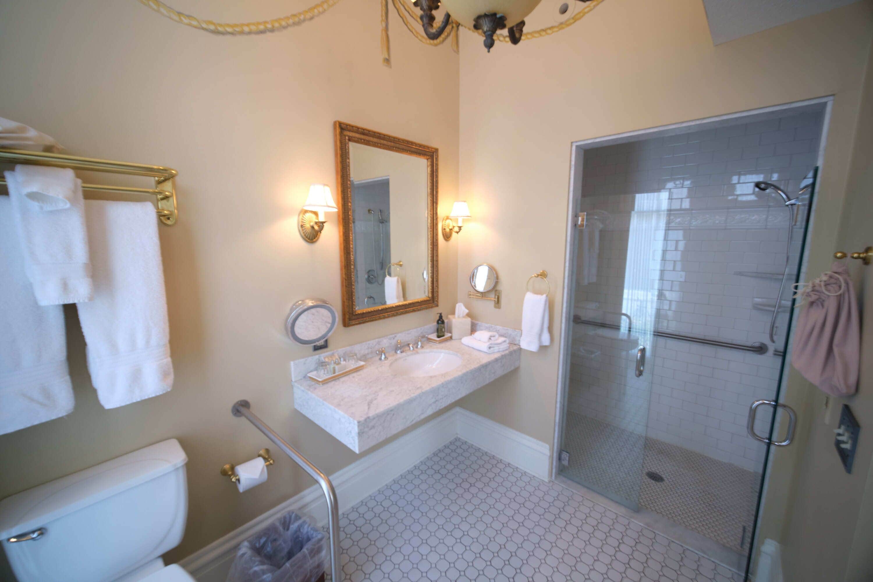 A bathroom with a marble sink, a large mirror, a glass shower enclosure, and a toilet.
