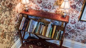 Une bibliothèque en bois, ornée de livres et de deux lampes, placée devant un mur recouvert d’un papier peint à motifs floraux.