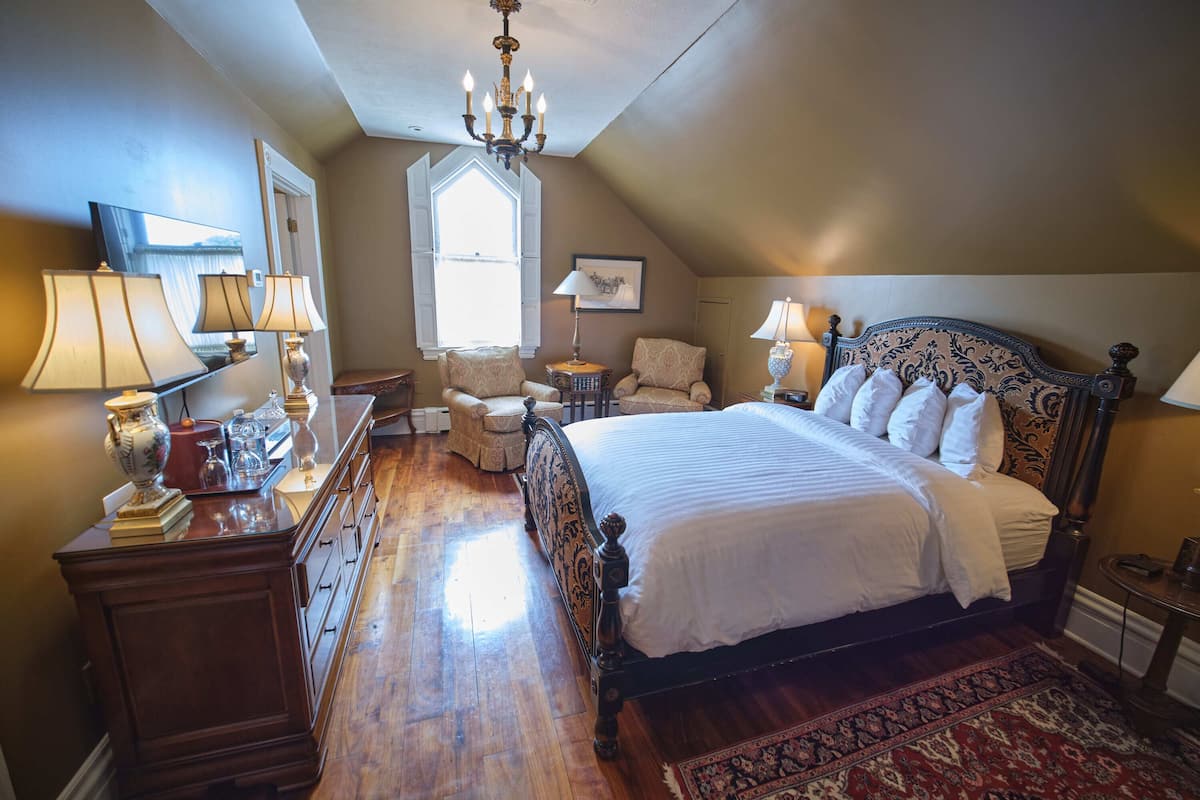 A bedroom with a large bed, a chandelier, a dresser, and a window with shutters.