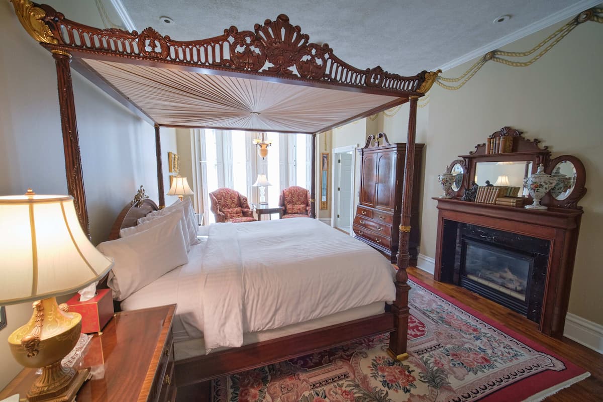 A four-poster bed with a canopy, a wooden dresser, a mirror, and a fireplace.