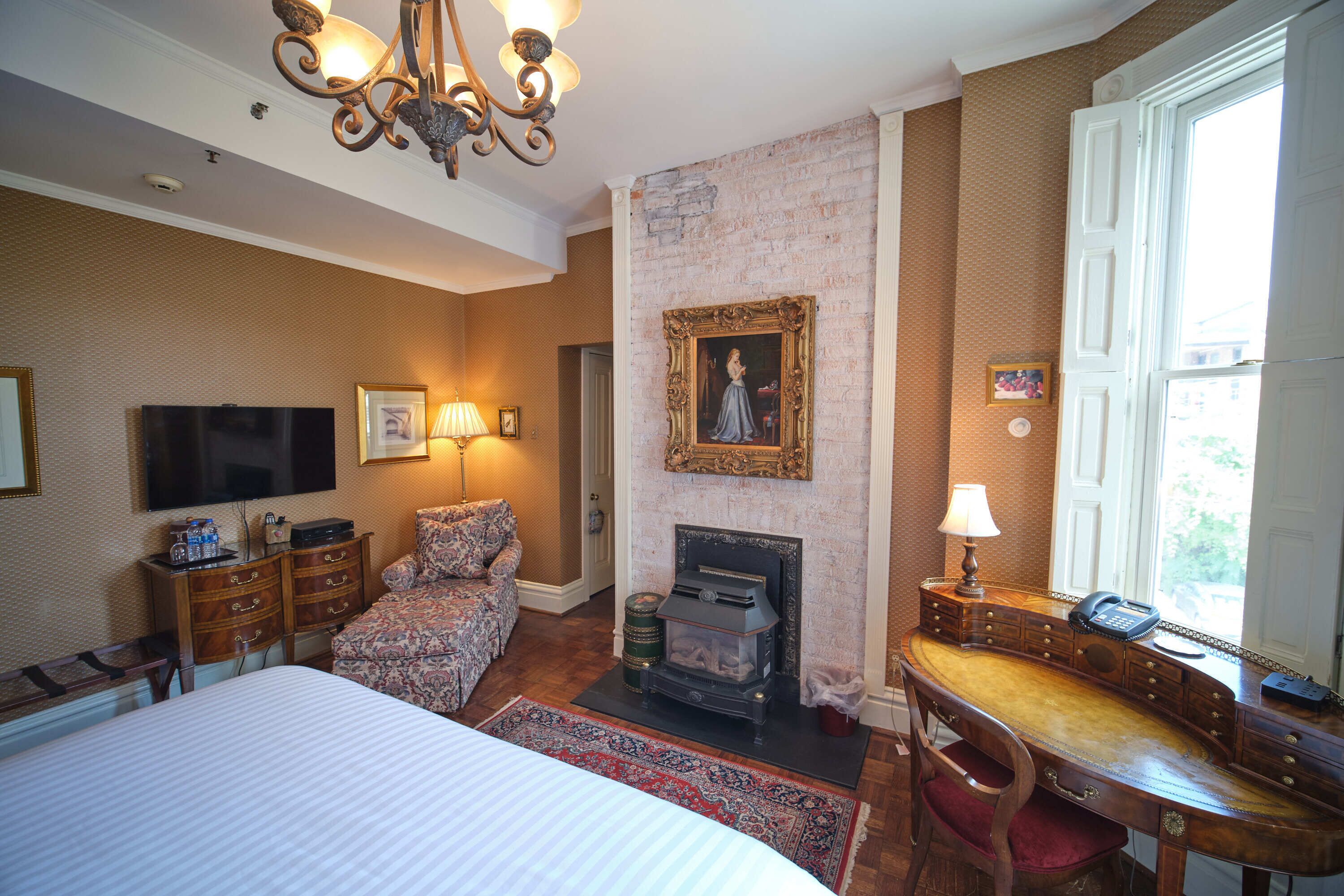 A hotel room with a bed, a desk with a telephone, a fireplace, and a television.