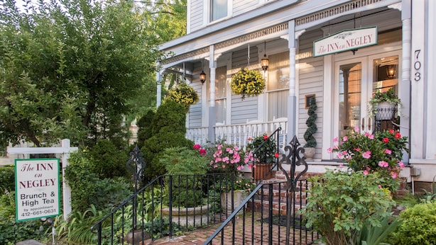 A white building with a porch, a sign for The Inn on Negley, and a brick staircase leading up to the entrance. - The Inn on Negley (Pittsburgh)