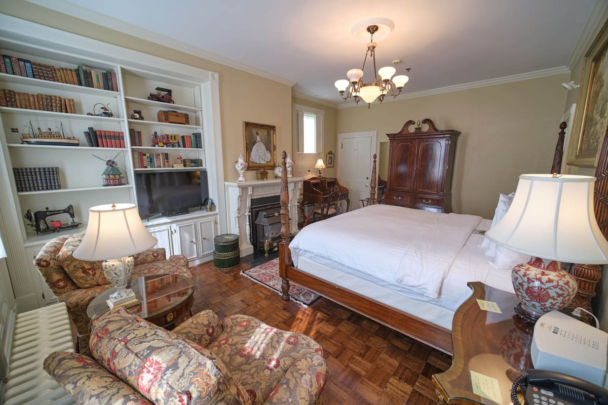 A bedroom with a large bed, a wooden wardrobe, a bookshelf, a fireplace, and a chandelier.