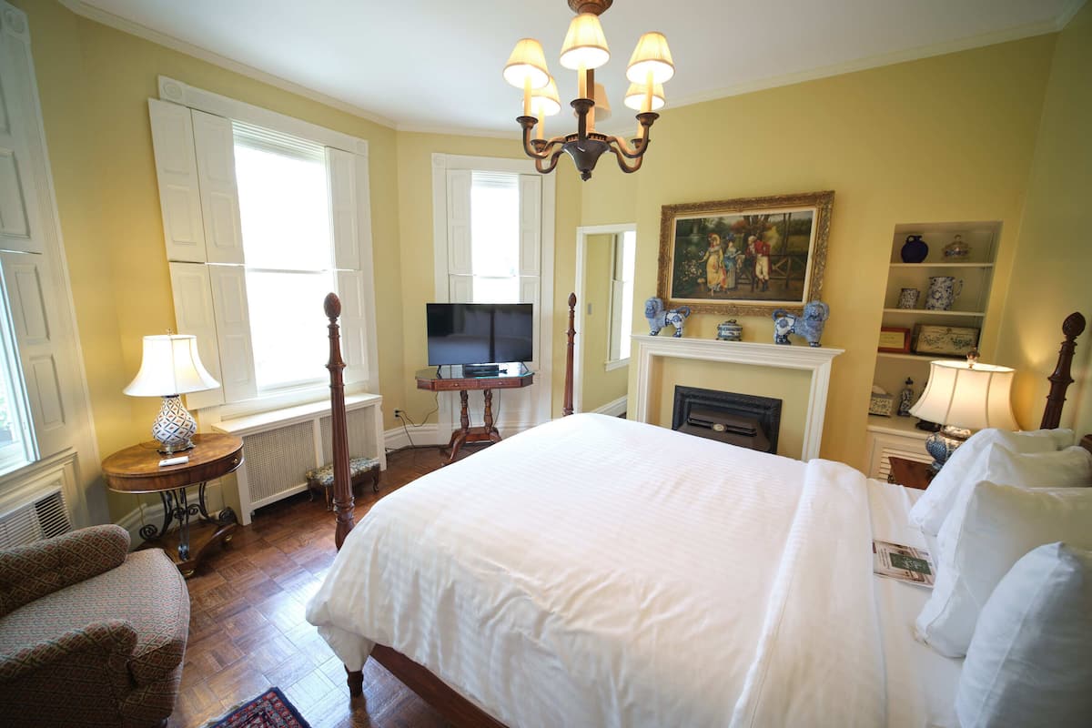 A well-lit bedroom with a large bed, a television, a fireplace, and a painting on the wall.