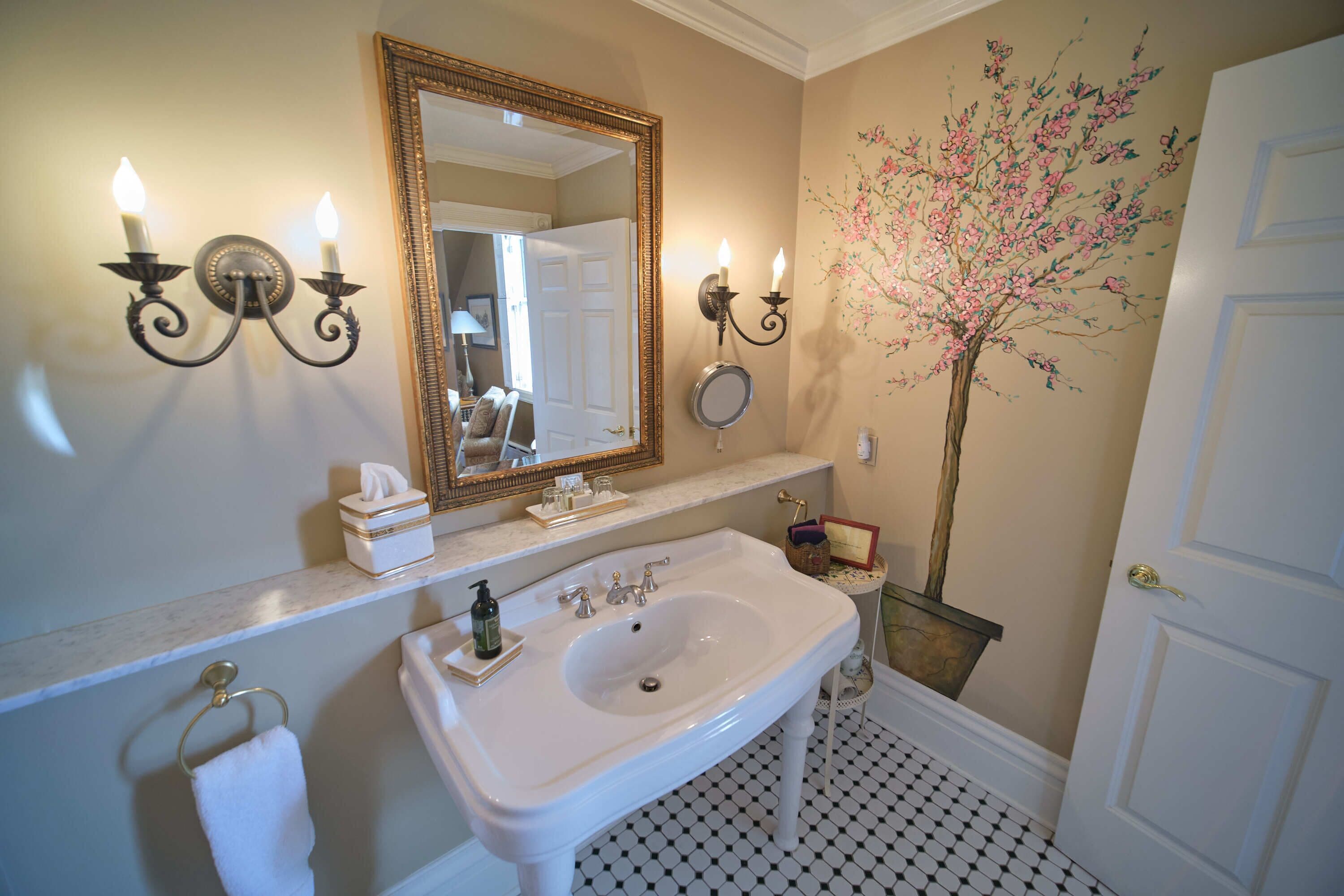 A bathroom with a white sink, two wall sconces, a large mirror, and a floral wall decoration.