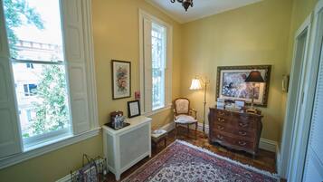 A room with a large window, a radiator, a chair, a dresser, and a rug.