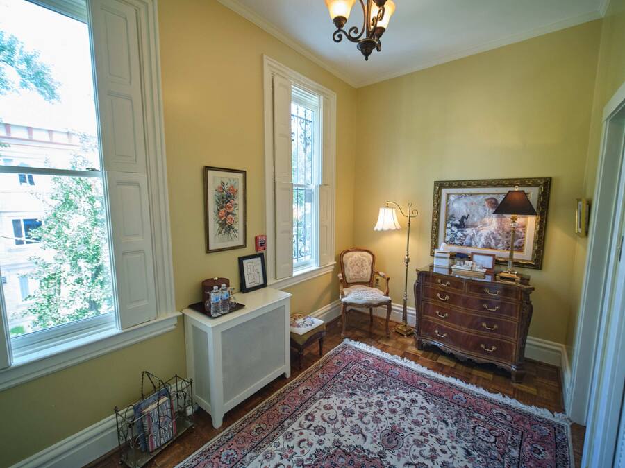 A room with a large window, a radiator, a chair, a dresser, and a rug.