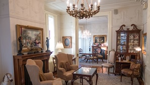 A spacious living room with a chandelier, multiple armchairs, a coffee table, and a wooden cabinet with glass doors. - The Inn on Negley (Pittsburgh)
