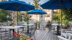 An outdoor patio with tables and chairs, blue umbrellas, and potted plants. - The Inn on Negley (Pittsburgh)