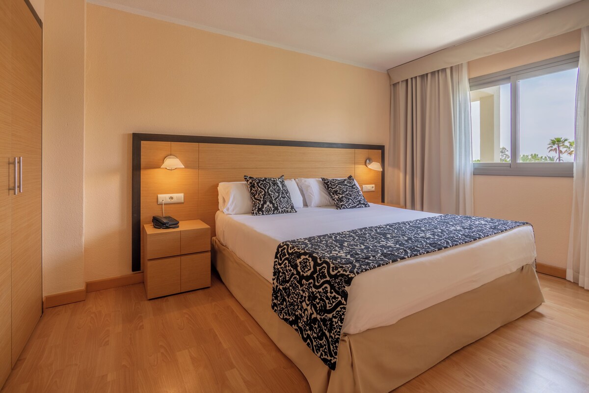 A hotel room with a large bed, bedside lamps, a nightstand, and a window with curtains.