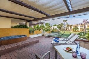 A wooden deck with a hot tub, lounge chairs, and a table with a plate of food and drinks.