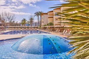 Uma piscina com tobogã, espreguiçadeiras, palmeiras e um edifício com varandas.