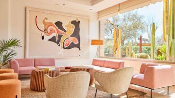 Una sala de estar moderna con un cuadro abstracto grande, un sofá rosa y vistas de cactus a través de amplias ventanas.