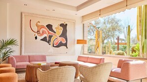 Una sala de estar moderna con un cuadro abstracto grande, un sofá rosa y vistas de cactus a través de amplias ventanas.