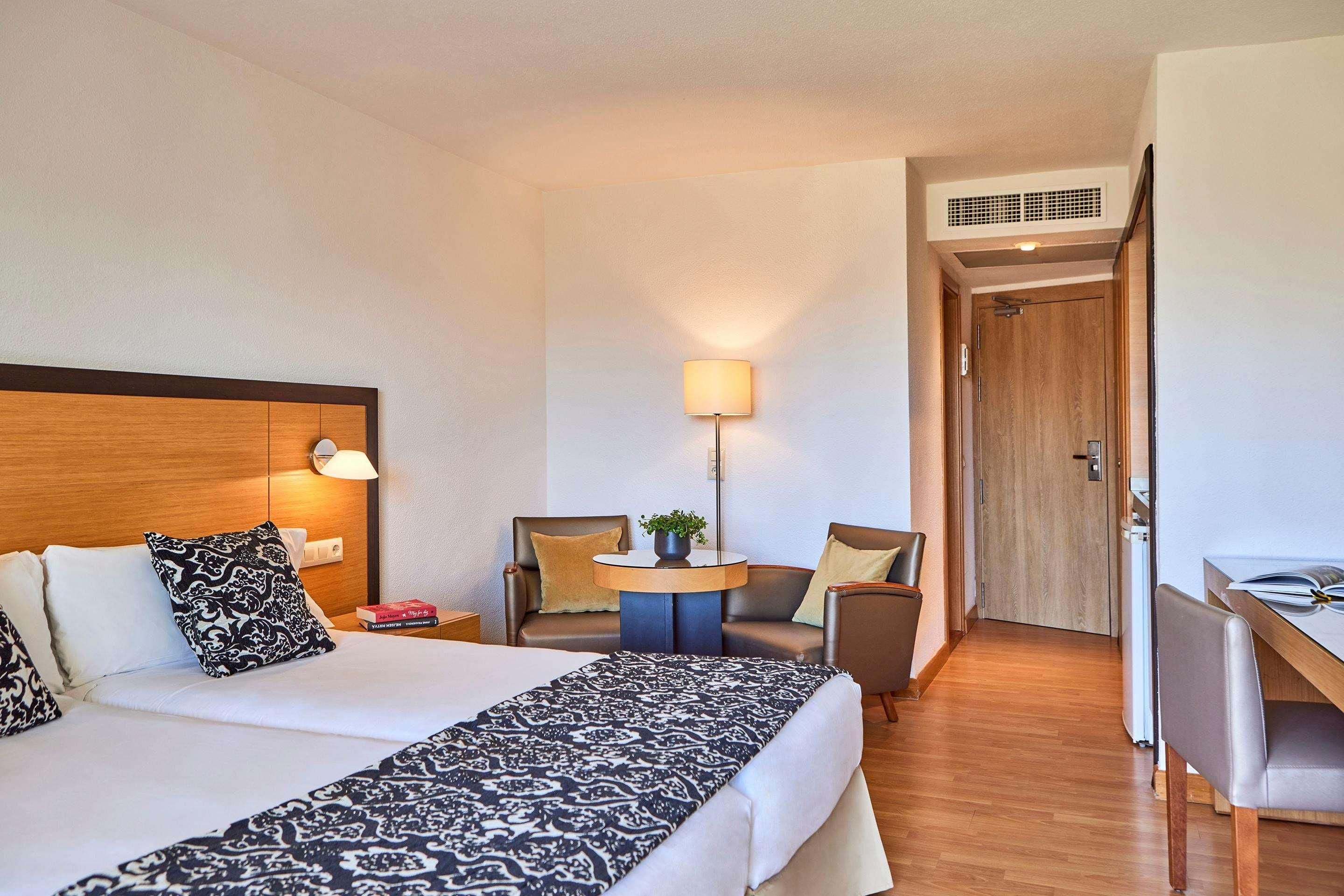 Una habitación de hotel con cama, dos sillas, escritorio y lámpara.