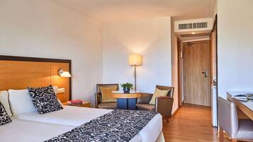 Una habitación de hotel con cama, dos sillas, escritorio y lámpara.