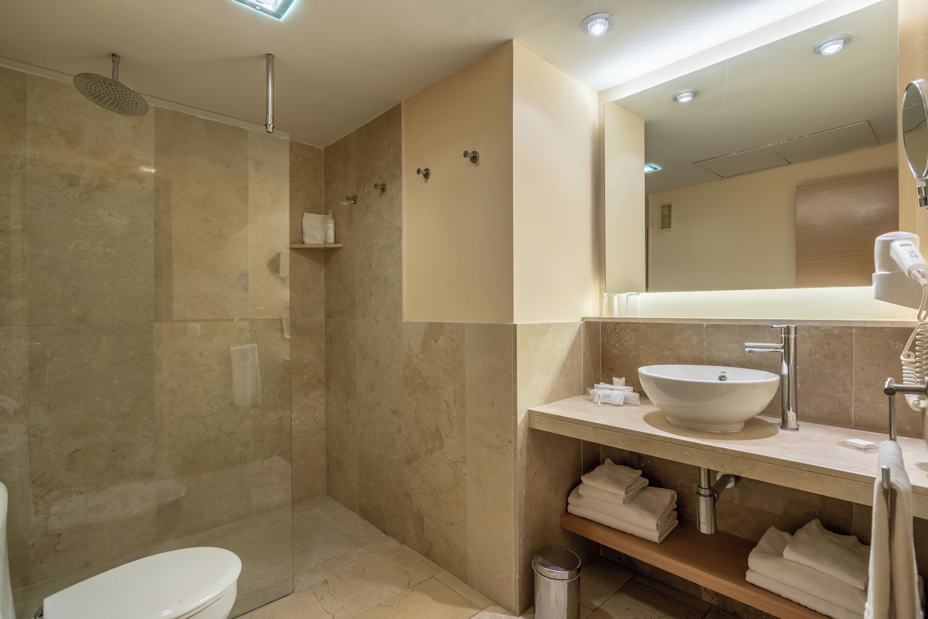Un baño moderno con ducha acristalada, lavamanos blanco y espejo sobre el mueble.
