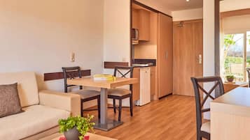 A modern living room with a sofa, a dining table with chairs, a small kitchen area, and a sliding door leading to an outdoor space.