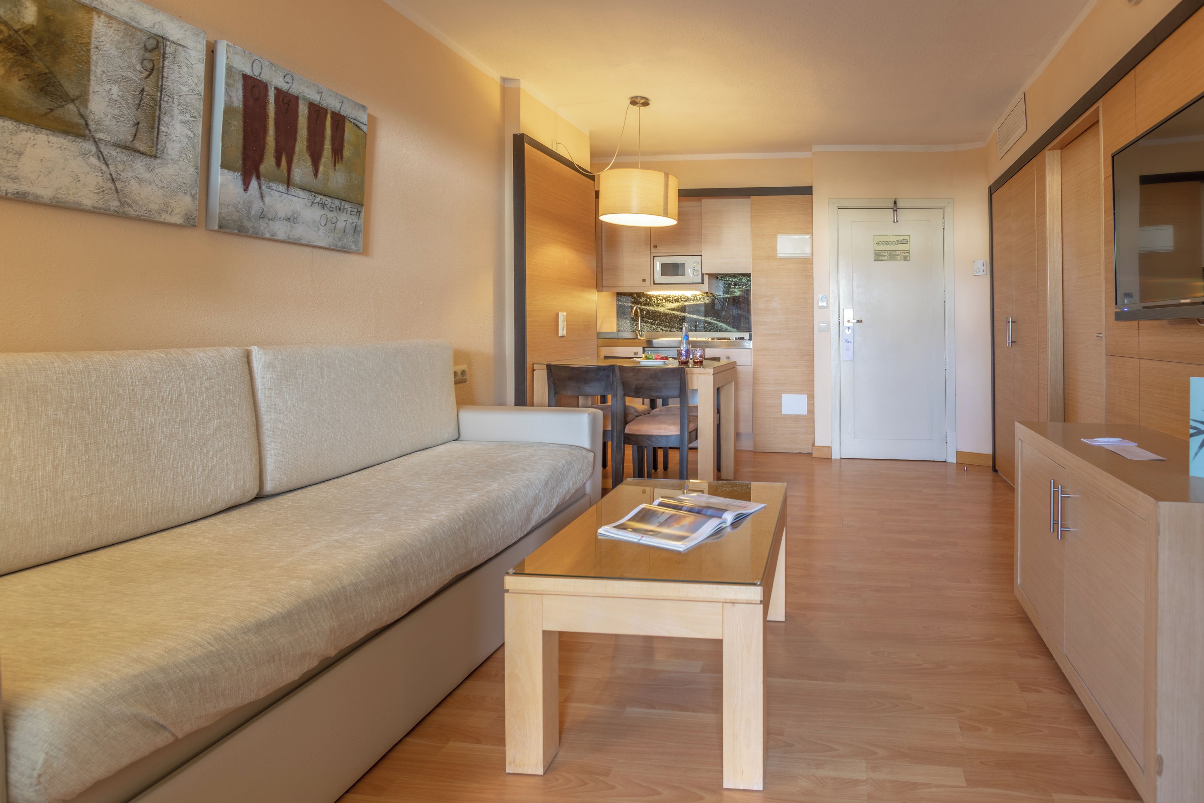 Una sala de estar moderna con un sofá, una mesa de centro y un comedor con sillas y una mesa. Hay una zona de cocina con un microondas y armarios.
