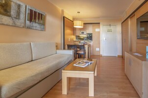 Una sala de estar moderna con un sofá, una mesa de centro y un comedor con sillas y una mesa. Hay una zona de cocina con un microondas y armarios.
