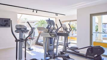 Un gimnasio con varias máquinas de ejercicio, un ventanal y vistas a palmeras.