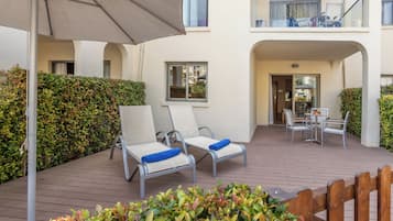 Eine Terrassenfläche mit zwei Liegestühlen, einem Tisch und einem großen Sonnenschirm.