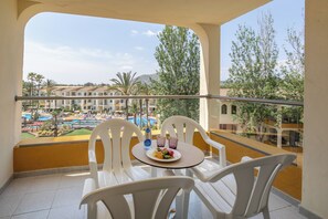A balcony with white plastic chairs and a small table, overlooking a pool area with multiple pools and palm trees. - Zafiro Tropic (Alcúdia)