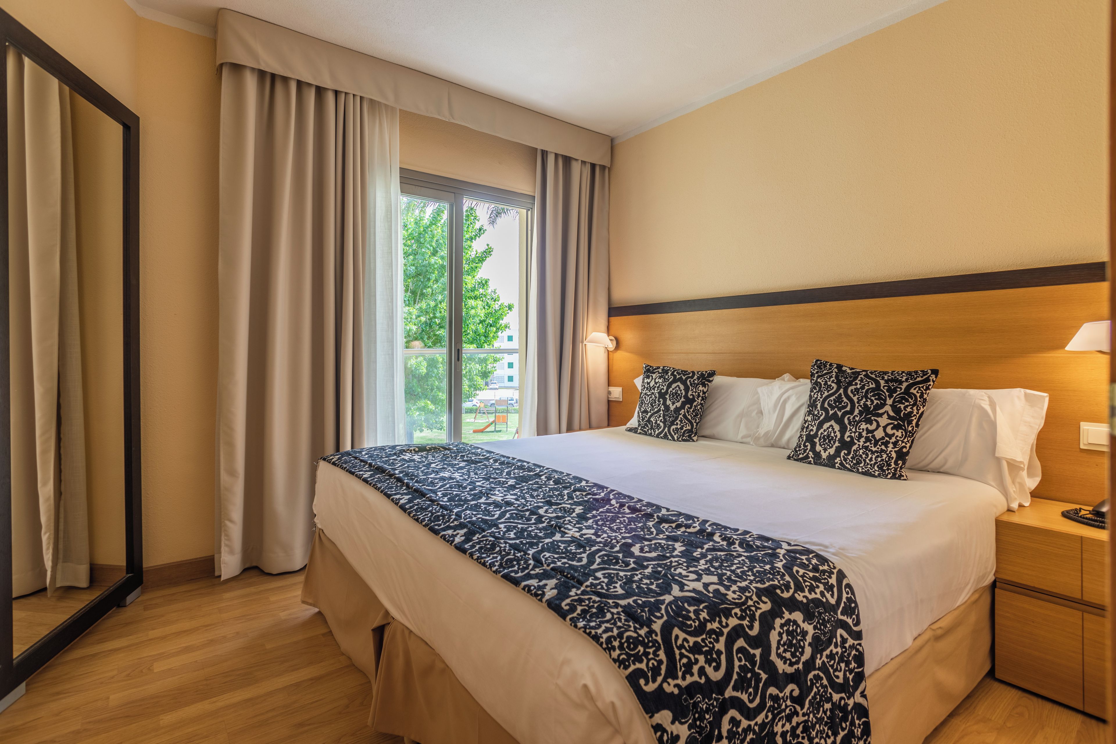 Habitación de hotel con una cama grande, dos lámparas de noche, una mesita y vistas al exterior.