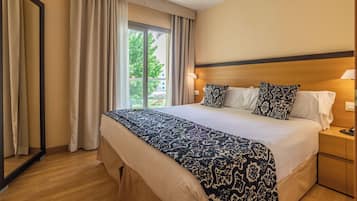 Habitación de hotel con una cama grande, dos lámparas de noche, una mesita y vistas al exterior.