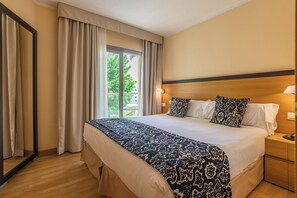 A hotel room with a large bed, two bedside lamps, a nightstand, and a view of the outdoors. - Zafiro Tropic (Alcúdia)