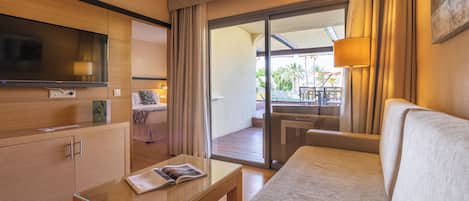 Habitación de hotel con sofá, una mesa de centro, televisor y puerta corrediza de vidrio que da a un espacio exterior.