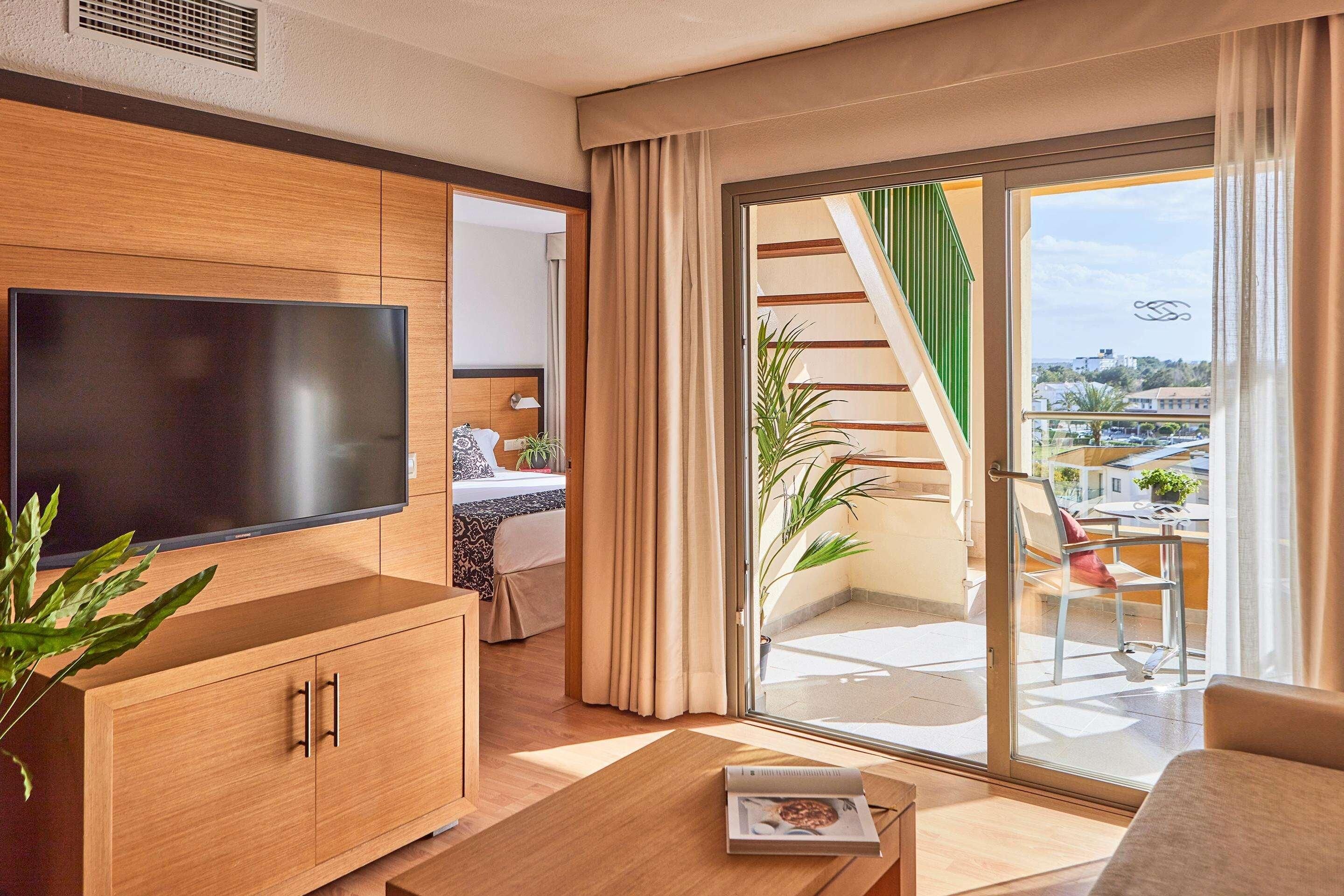 Ein modernes Hotelzimmer mit einem großen Flachbildfernseher, Holzmöbeln, einem Balkon mit Blick und einer Schiebetür aus Glas.