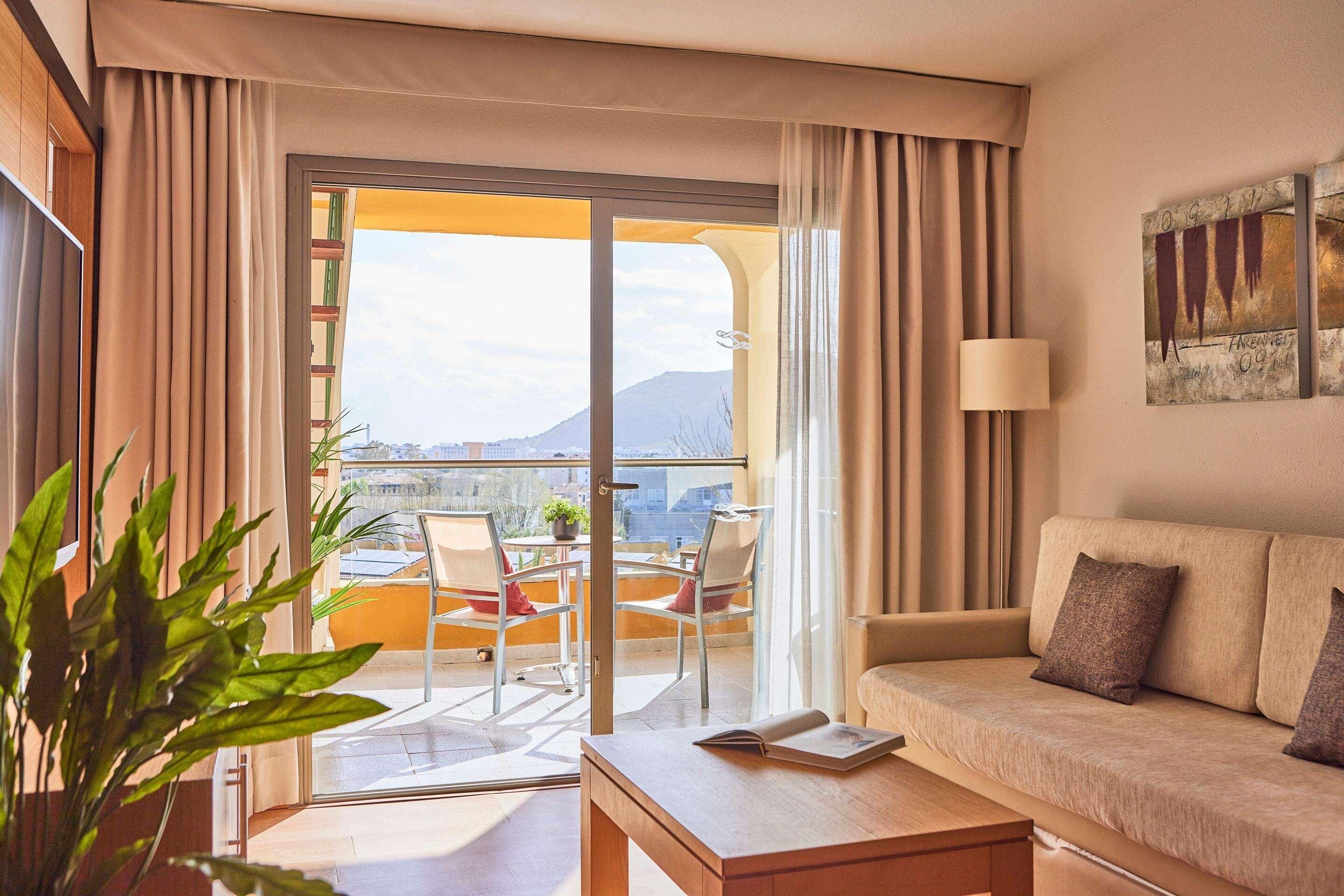 Ein modernes Hotelzimmer mit Balkon, einer Sitzecke, einem Tisch und Blick auf die Stadt.
