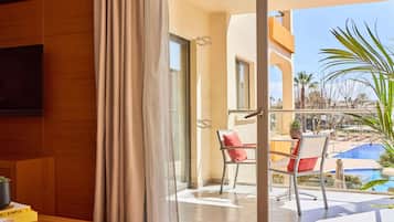 Een hotelkamer met balkon, een eettafel en een stoel met een rode kussen.