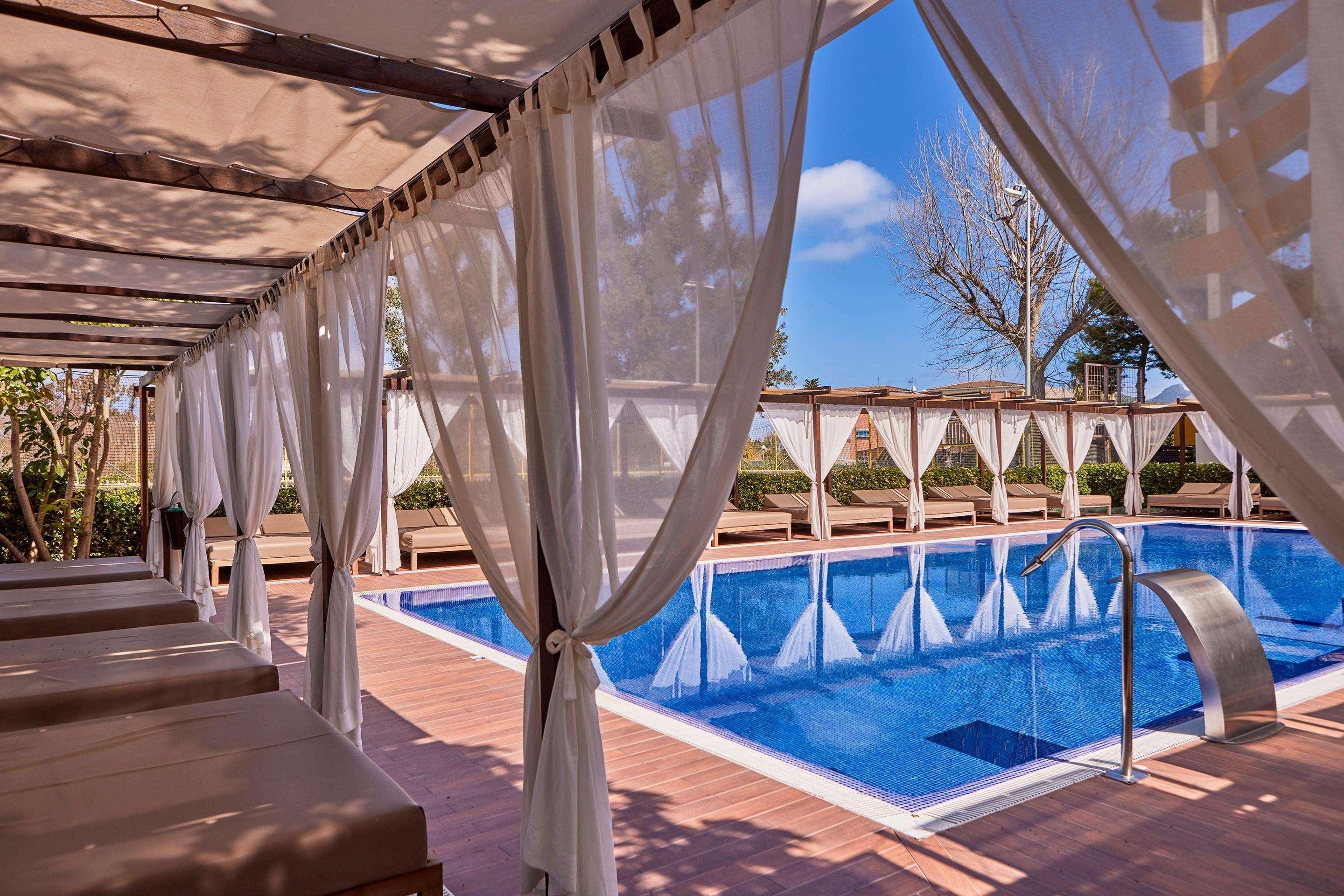 Un área de piscina con vista despejada, sillones de descanso y una pérgola con cortinas blancas.