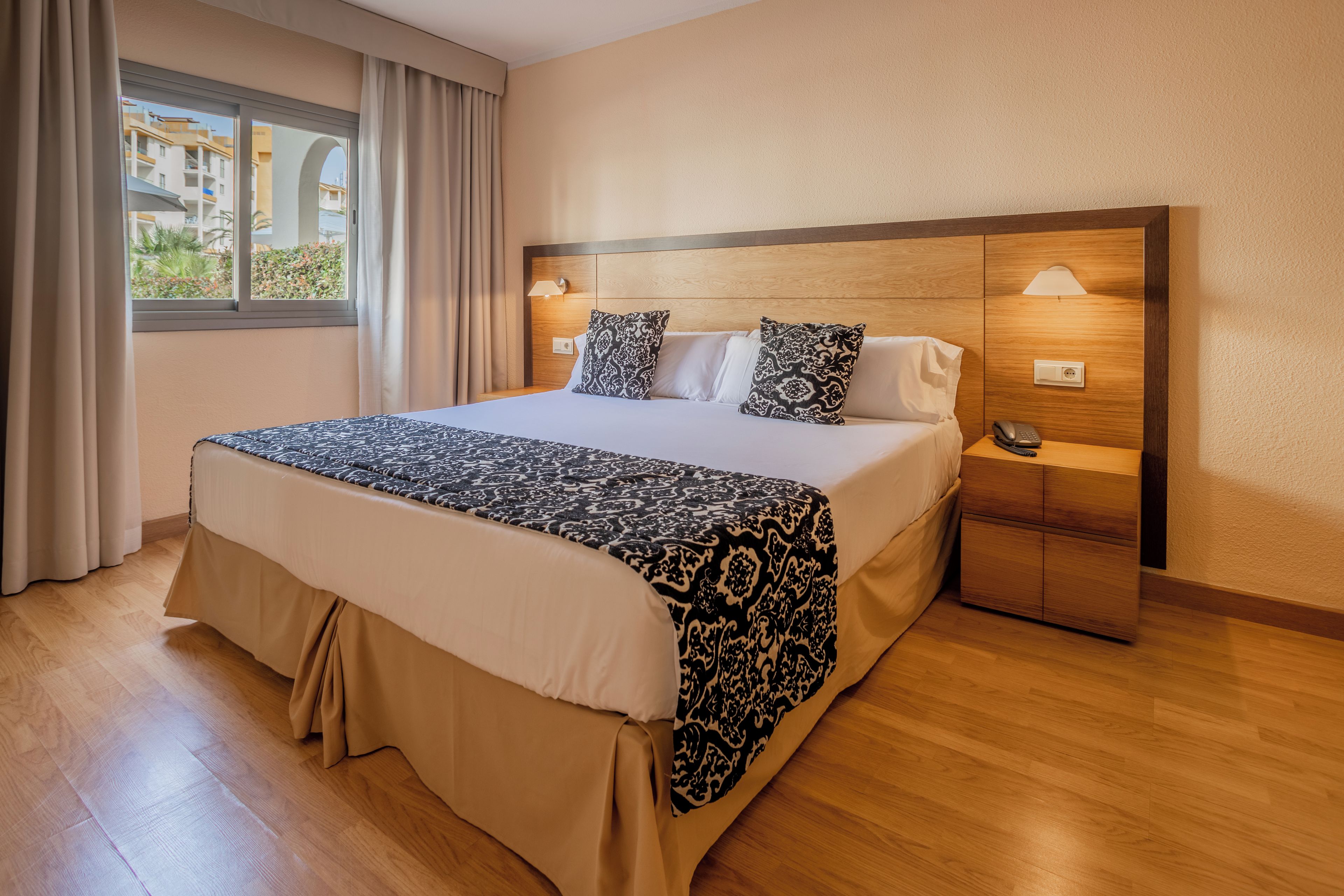 Une chambre d’hôtel avec un grand lit, une table de chevet avec une lampe et une vue sur les bâtiments à travers la fenêtre.