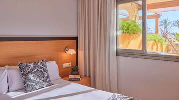 Habitación de hotel con cama, mesita de noche con lámpara, ventana con cortinas y vista a zonas verdes.
