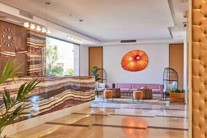 A modern lobby with a marble reception desk, a large wall clock, a unique umbrella artwork, and a plush seating area.