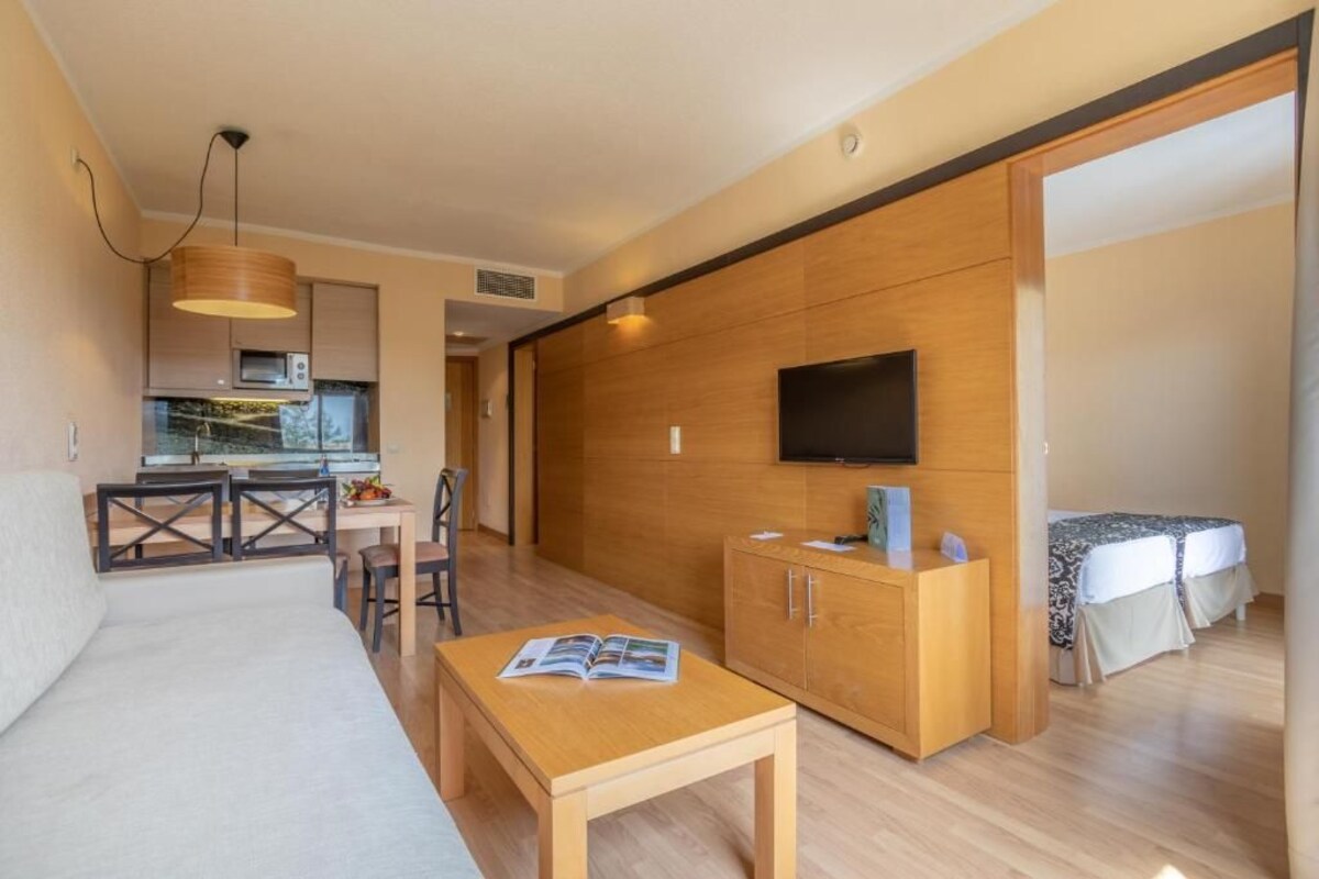 A modern living room with a sofa, a dining table, a TV, and a kitchen area with a microwave.