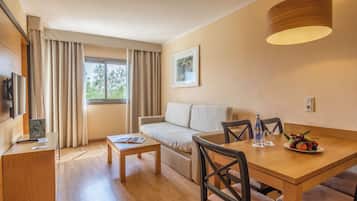 Habitación de hotel moderna con una mesa de comedor de madera, un sofá, una pequeña mesa de centro, un televisor y una ventana con cortinas.