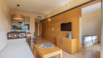 Una sala de estar moderna con un sofá, una mesa de comedor con sillas, una zona de cocina con microondas y un televisor montado en la pared.