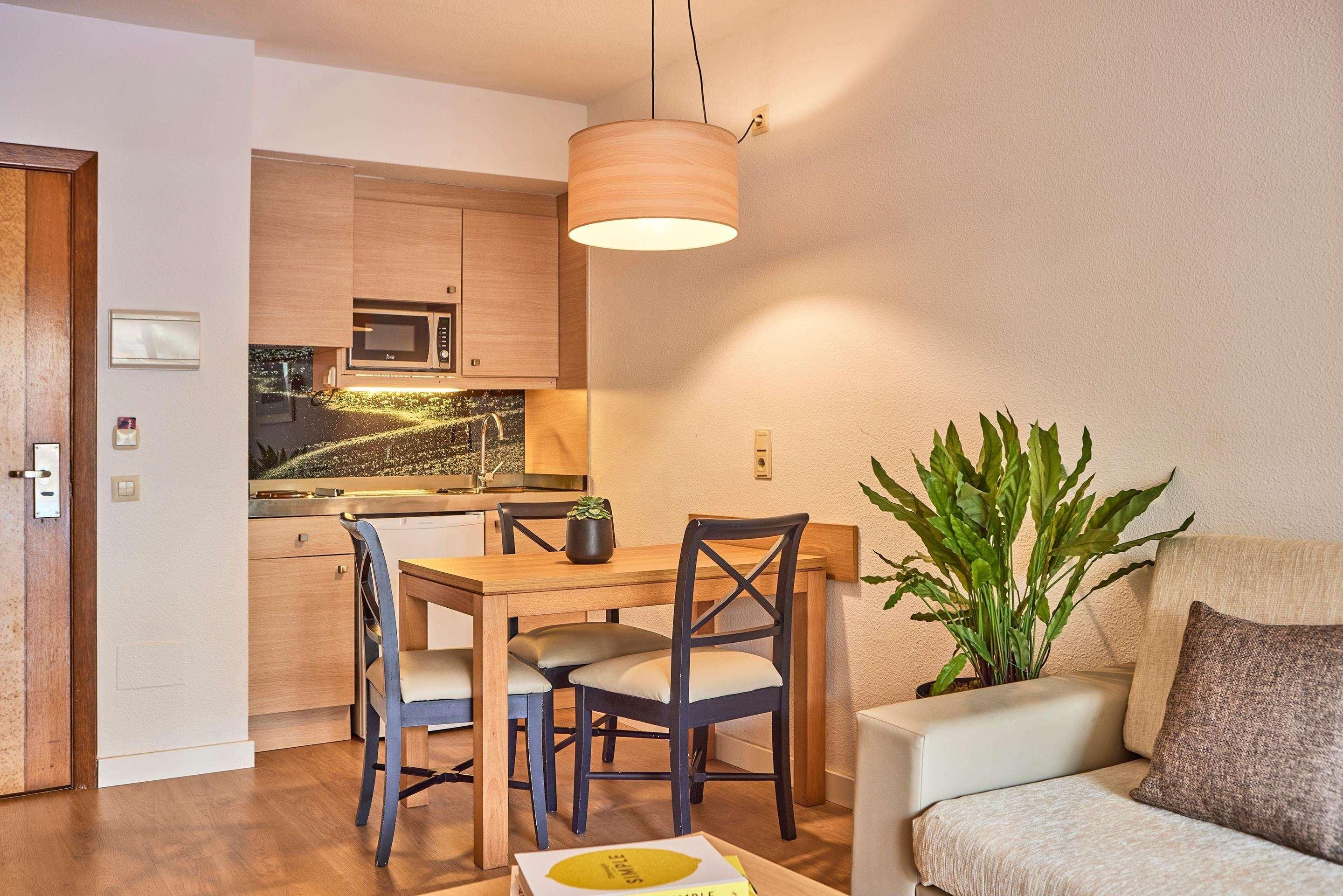 Un espacio habitable compacto con comedor, kitchenette y una zona de estar con una planta.