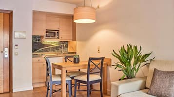 Un espacio habitable compacto con comedor, kitchenette y una zona de estar con una planta.