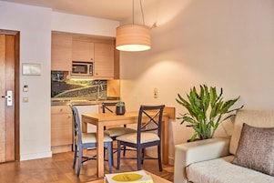 Un espacio habitable compacto con comedor, kitchenette y una zona de estar con una planta.