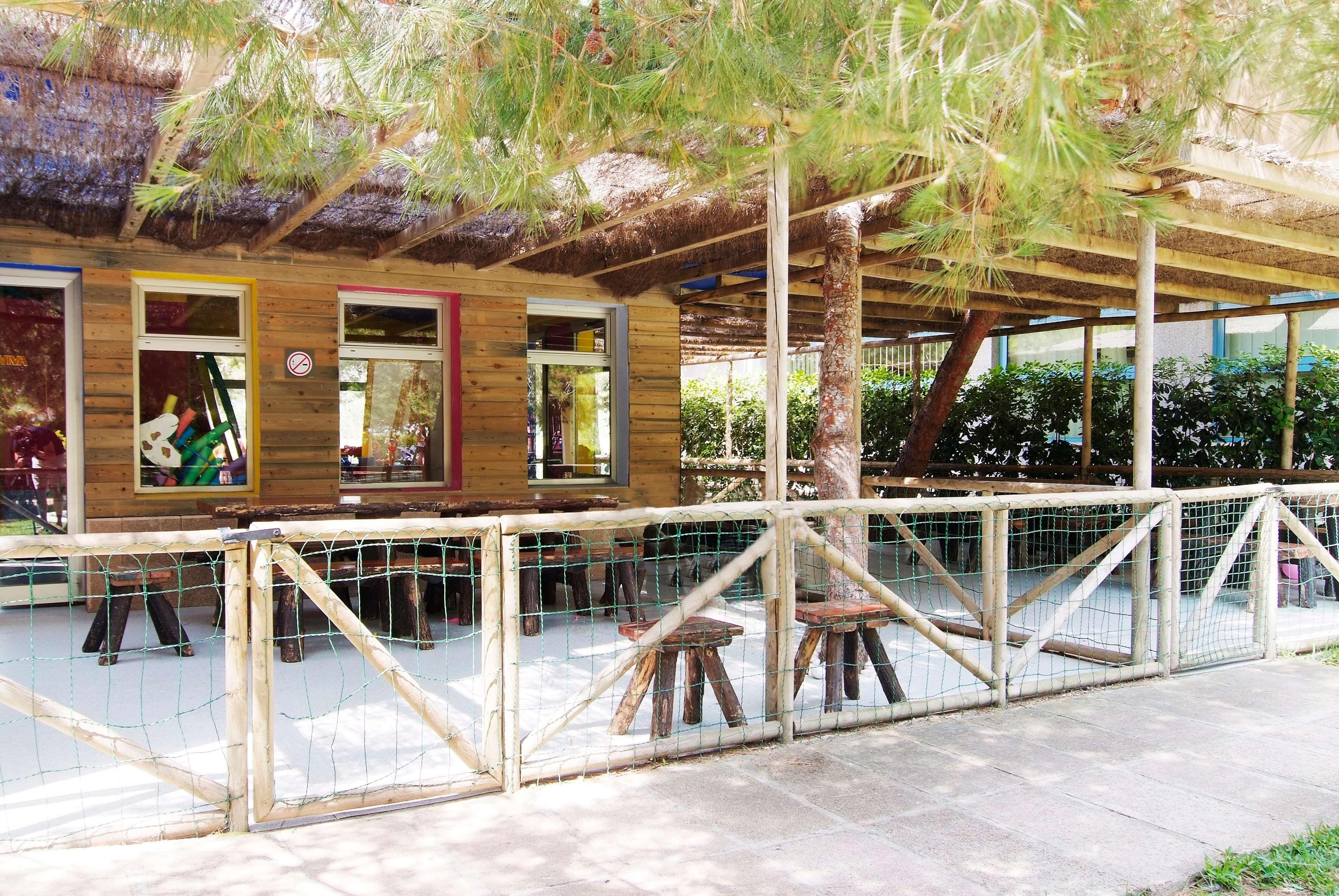 Una estructura de madera con techo de paja, bancos de madera y una zona vallada.