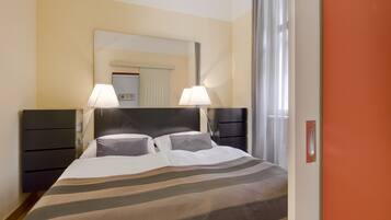 A hotel room with a bed, two bedside lamps, a nightstand, a mirror, and a window with curtains.