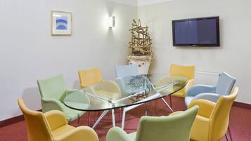 Un salón de conferencias con una mesa de vidrio rodeada de sillas coloridas, un televisor montado y una escultura decorativa.