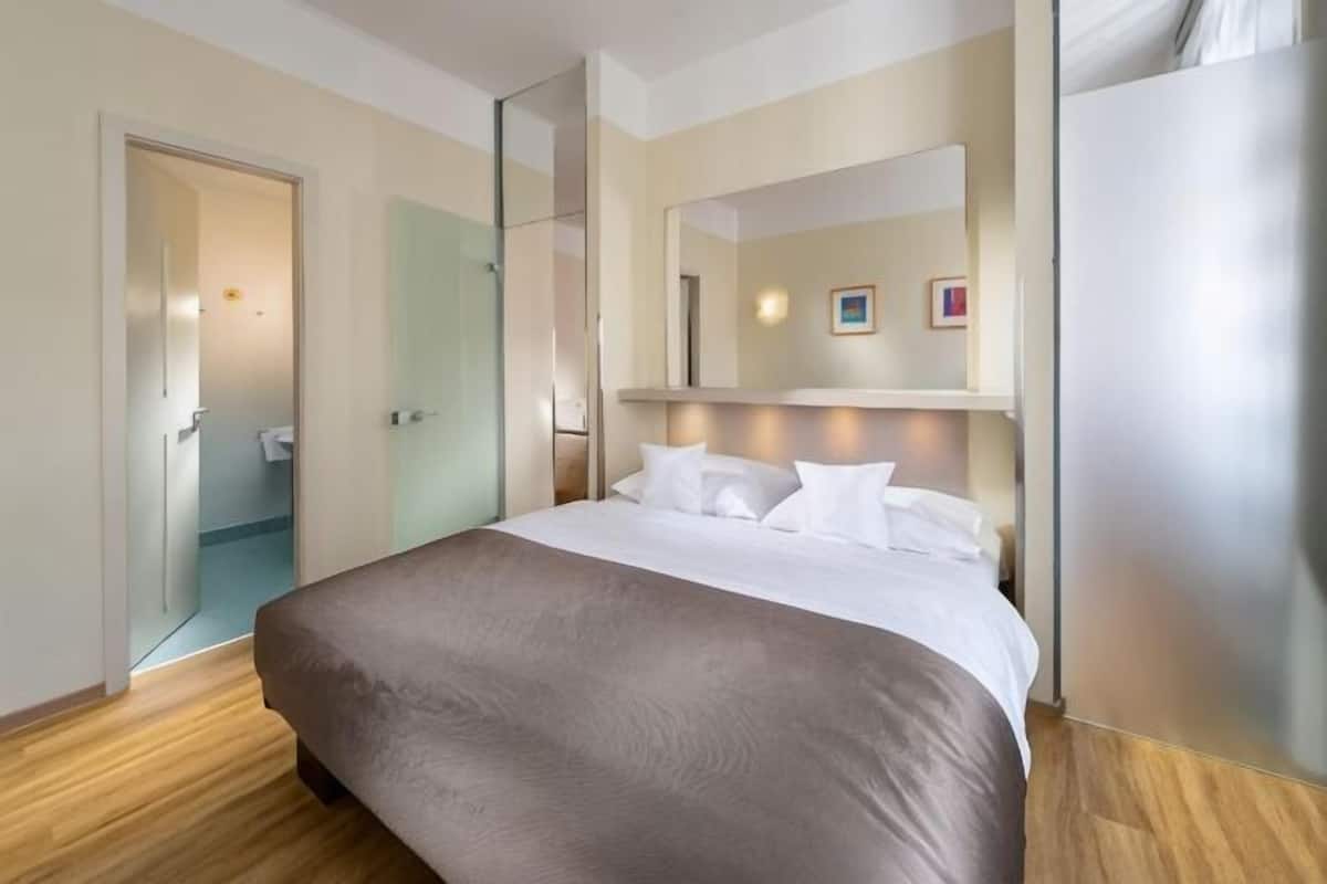 Habitación de hotel con cama, espejo, puerta y suelo de madera.