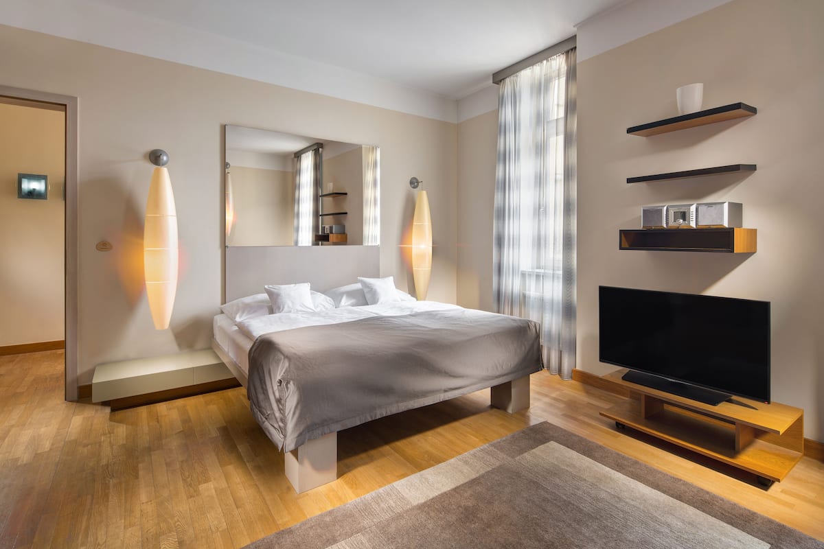 Una habitación de hotel moderna con una cama grande, un televisor de pantalla plana, estanterías empotradas y un espejo amplio.